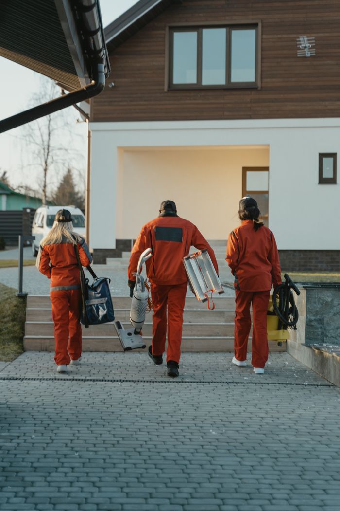 Équipe de nettoyage en uniformes rouges, équipée, s’approchant de l’extérieur d’une maison moderne.